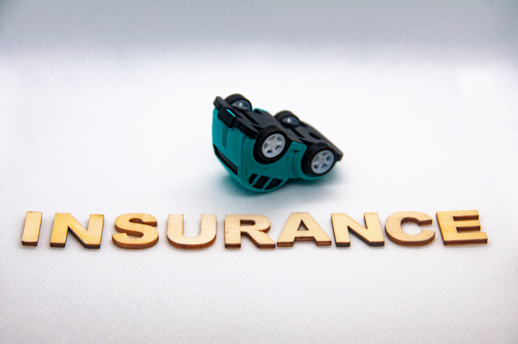 Insurance wooden text and model car turning up-side-down.